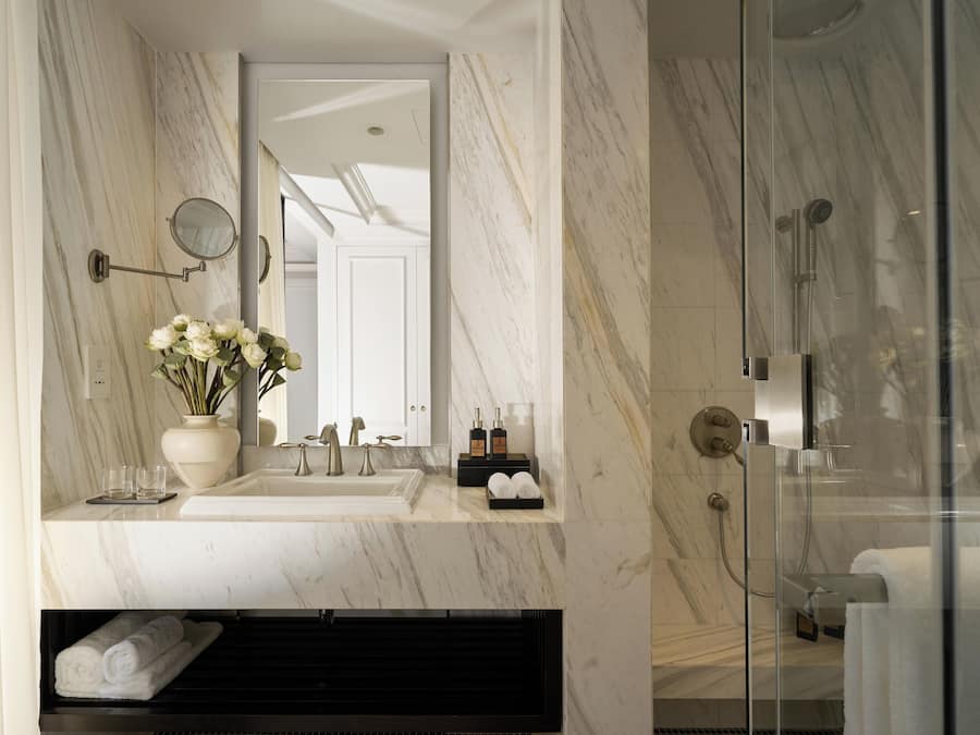 A modern bathroom with a marble sink, a mirror, a glass-enclosed shower, and a towel rack.