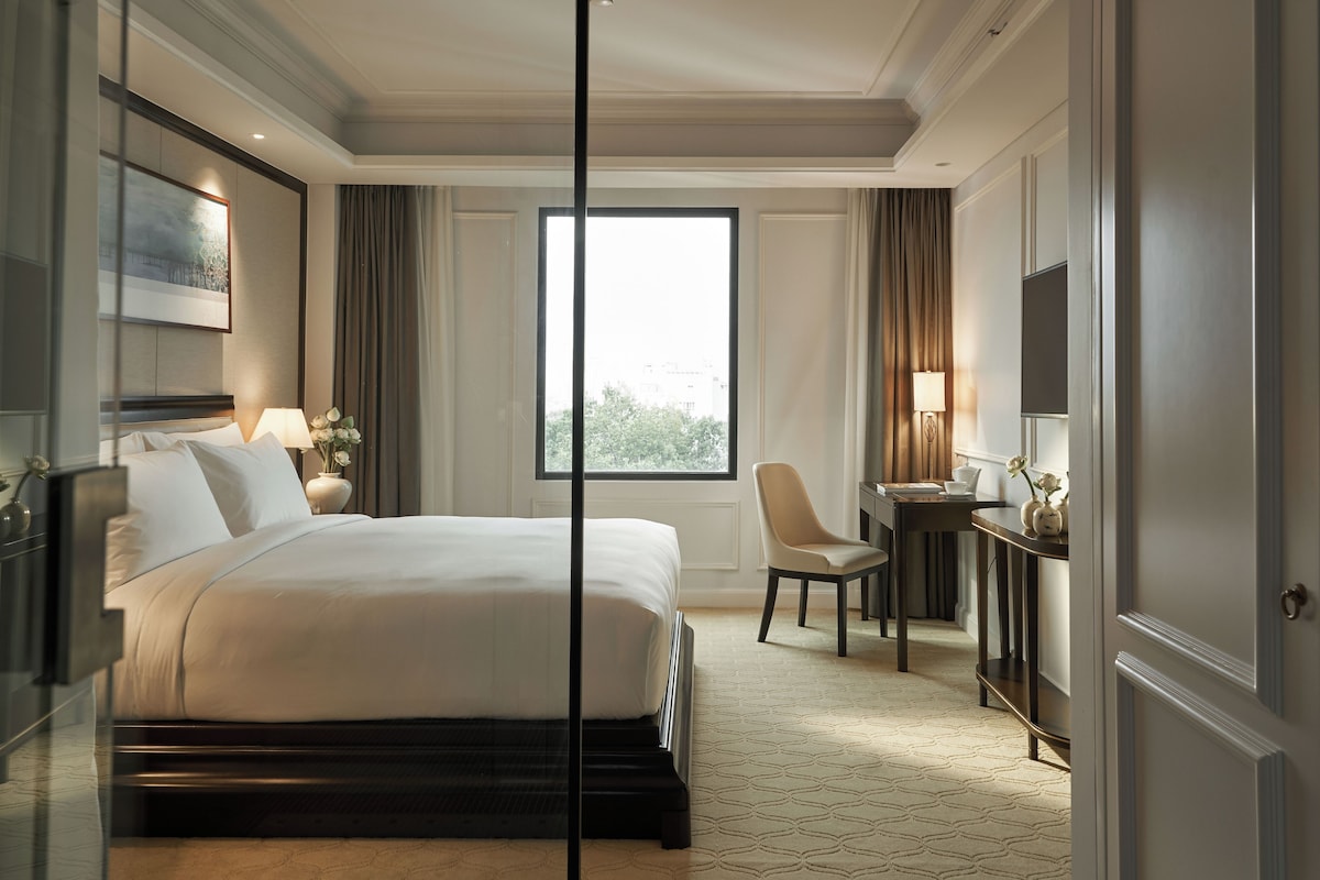 Une chambre d’hôtel avec un grand lit, un bureau, une chaise et une fenêtre donnant sur un beau paysage.