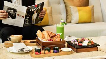 Una persona legge una rivista Forbes, una tazza di caffè, croissant, succo verde e un vassoio per la colazione con marmellate e burro.