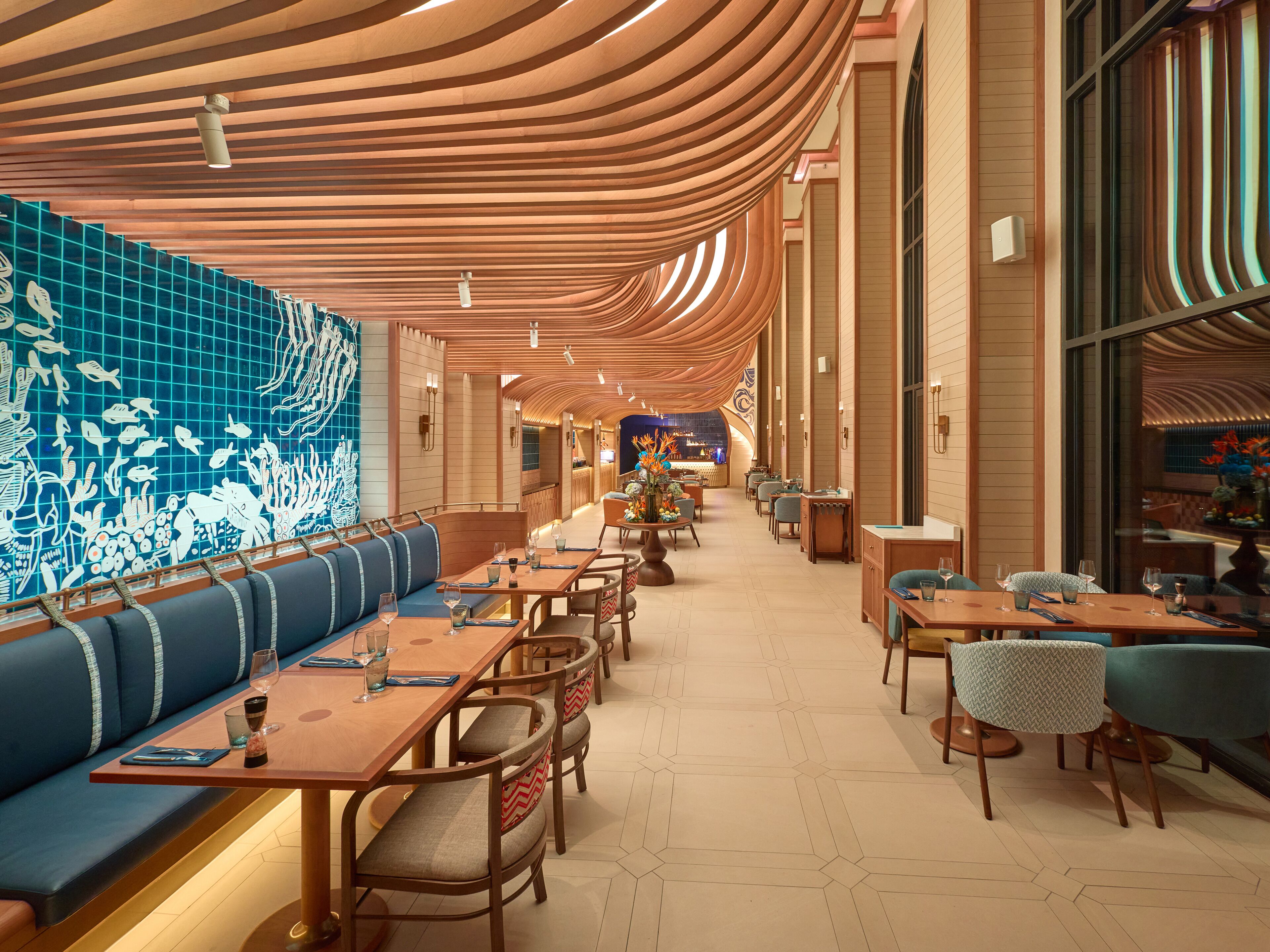 Un ristorante con pannelli in legno al soffitto, sedute blu e una parete piastrellata con decorazioni a tema marino.