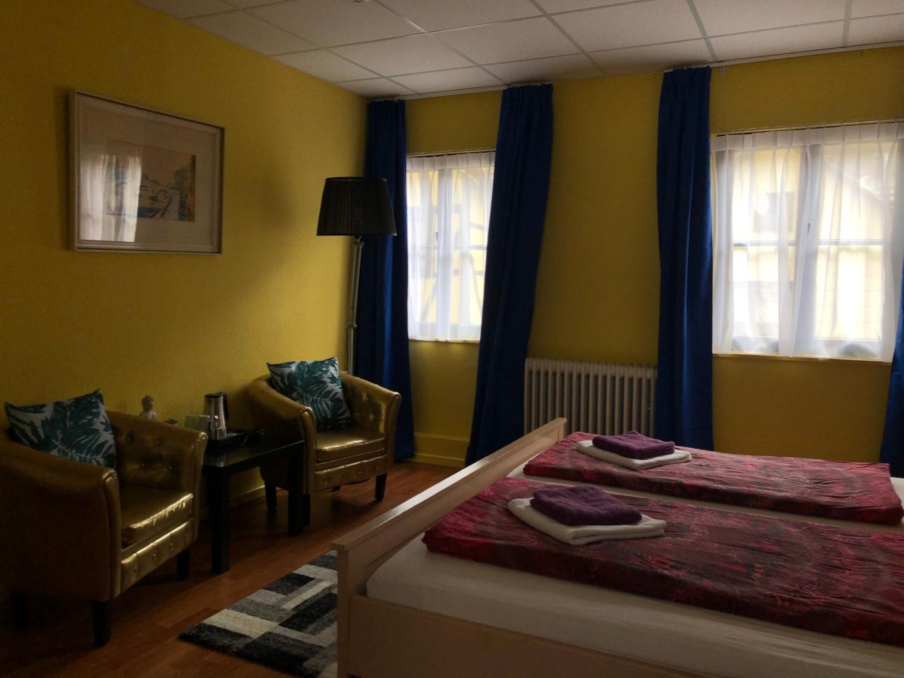 A room with two beds, a desk, a chair, and a floor lamp.