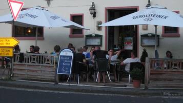 Restaurante com mesas ao ar livre, um anúncio para a cerveja Gerolsteiner e um quadro de cardápio.