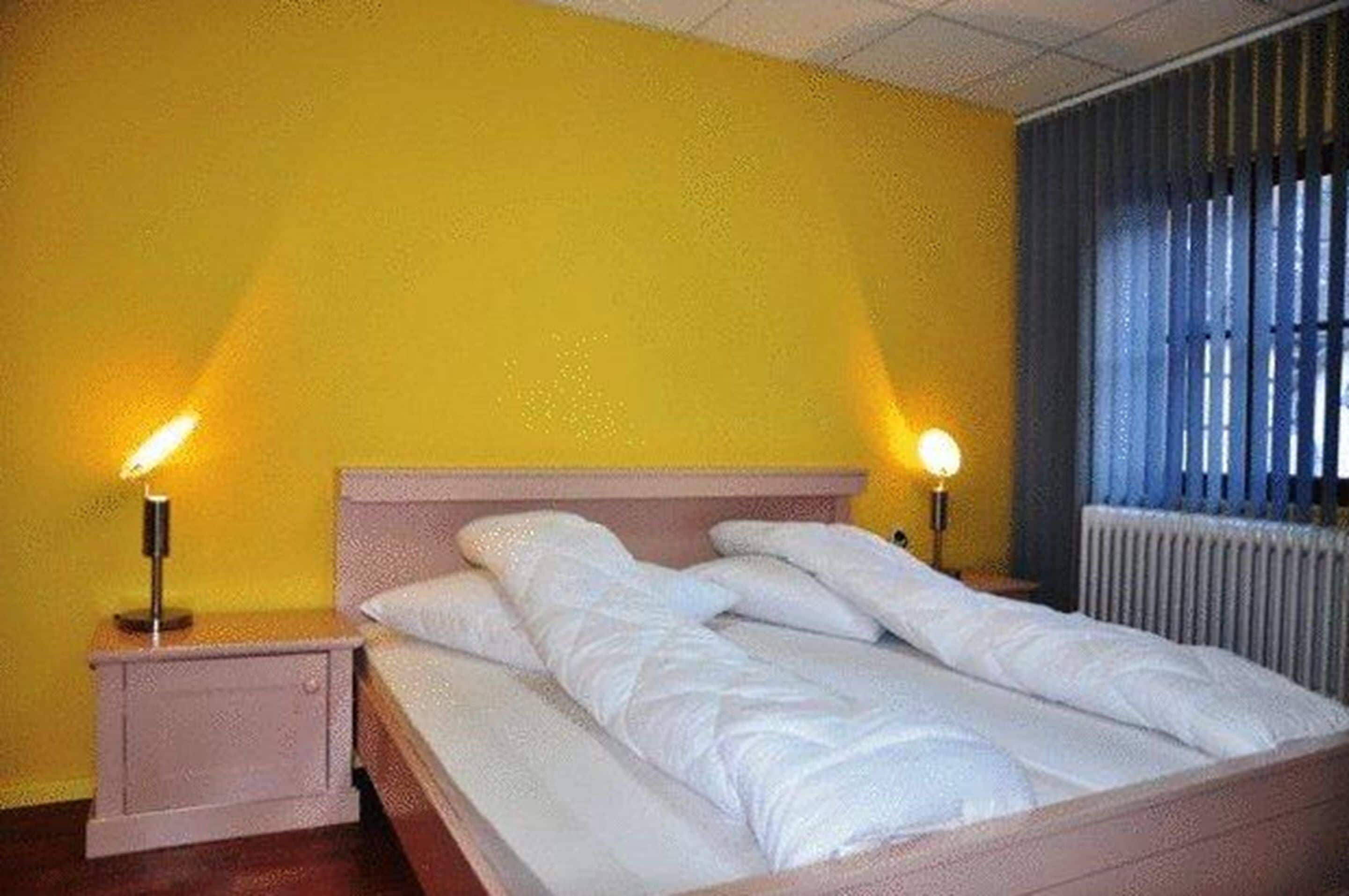 Un lit avec une literie blanche, dans une pièce aux murs jaunes et dotée d’un radiateur.