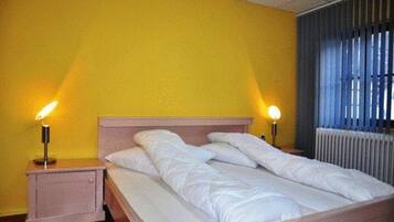Un lit avec une literie blanche, dans une pièce aux murs jaunes et dotée d’un radiateur.