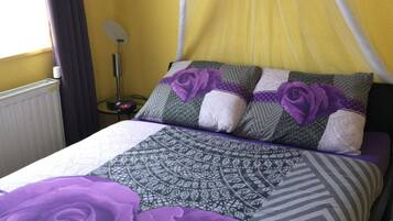 Un lit avec une couvre-lit à motifs violets et gris, une rose violette en guise de décoration et un oreiller blanc.