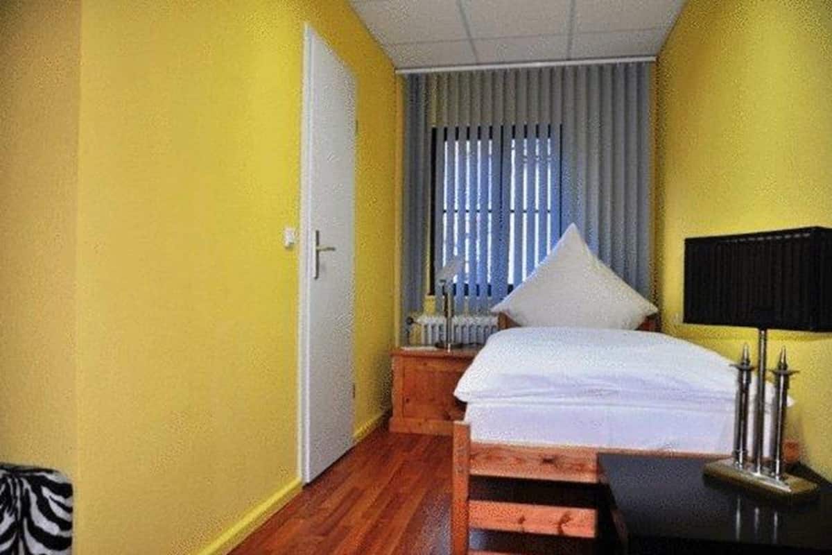A room with yellow walls, a wooden bed, a radiator, and a black lamp on a bedside table.