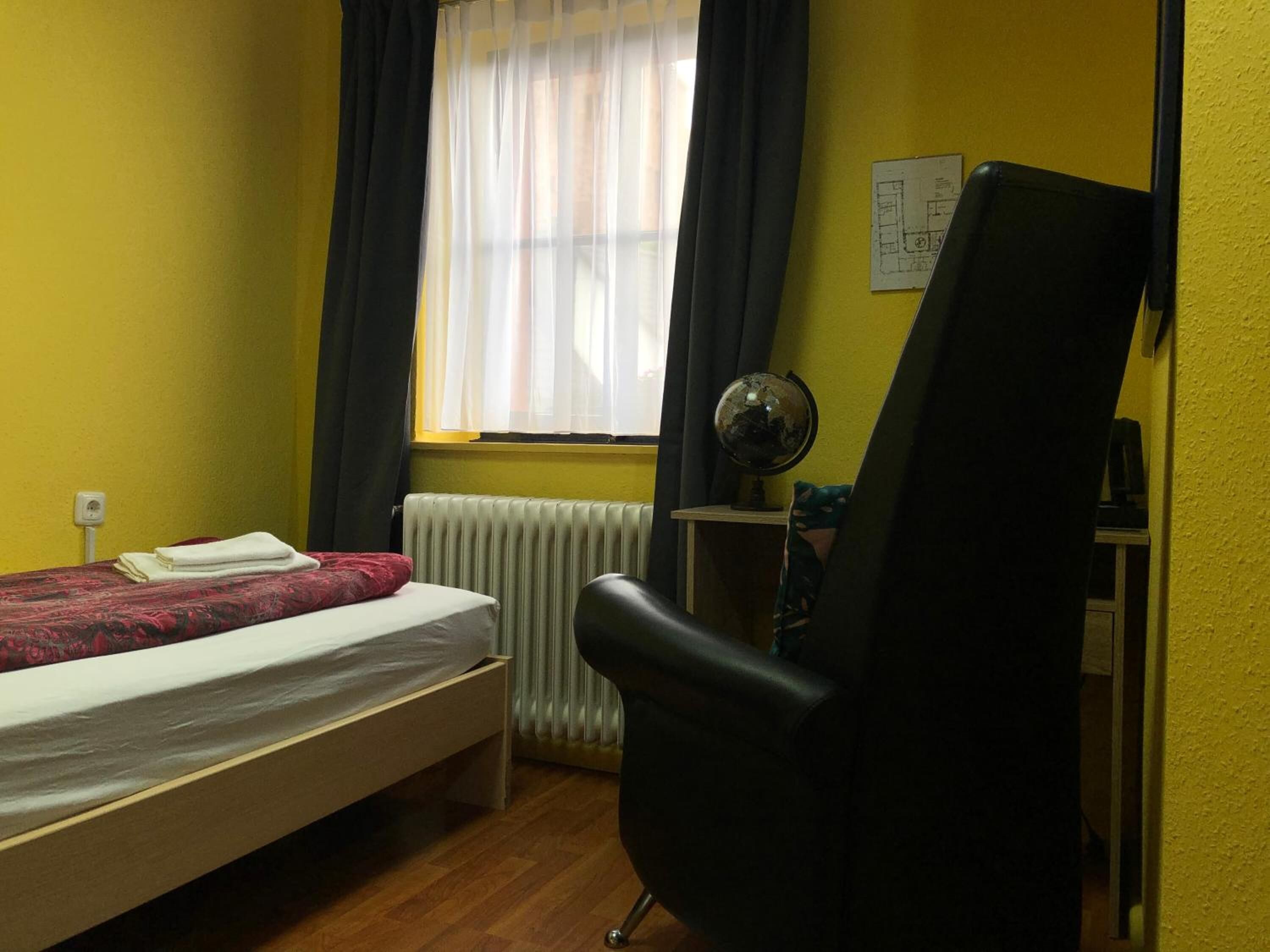 Una habitación pequeña con cama, escritorio, silla, un globo terráqueo y ventana con cortinas.