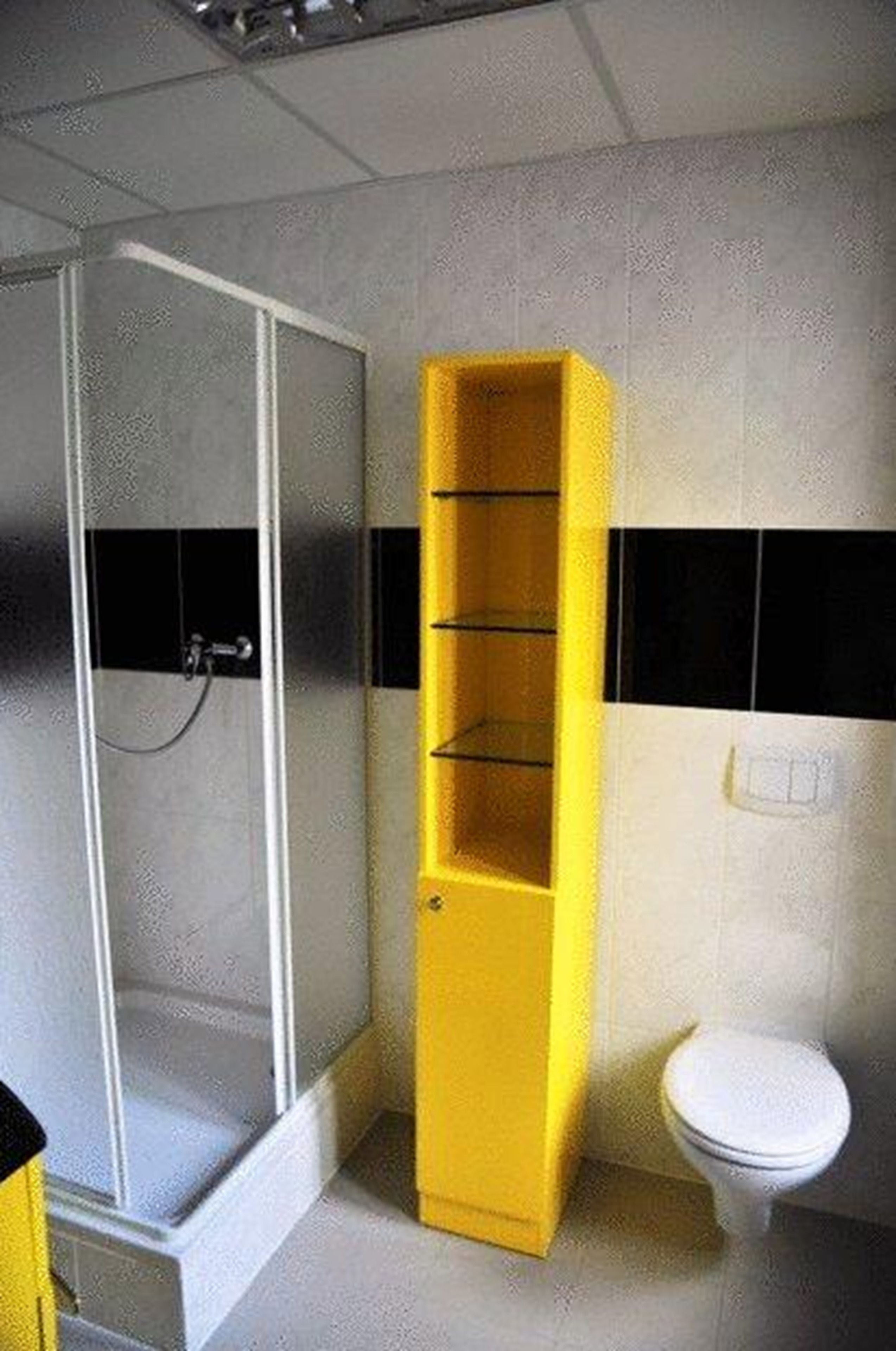 Un baño con cabina de ducha de vidrio, un mueble de almacenamiento amarillo y un inodoro blanco.