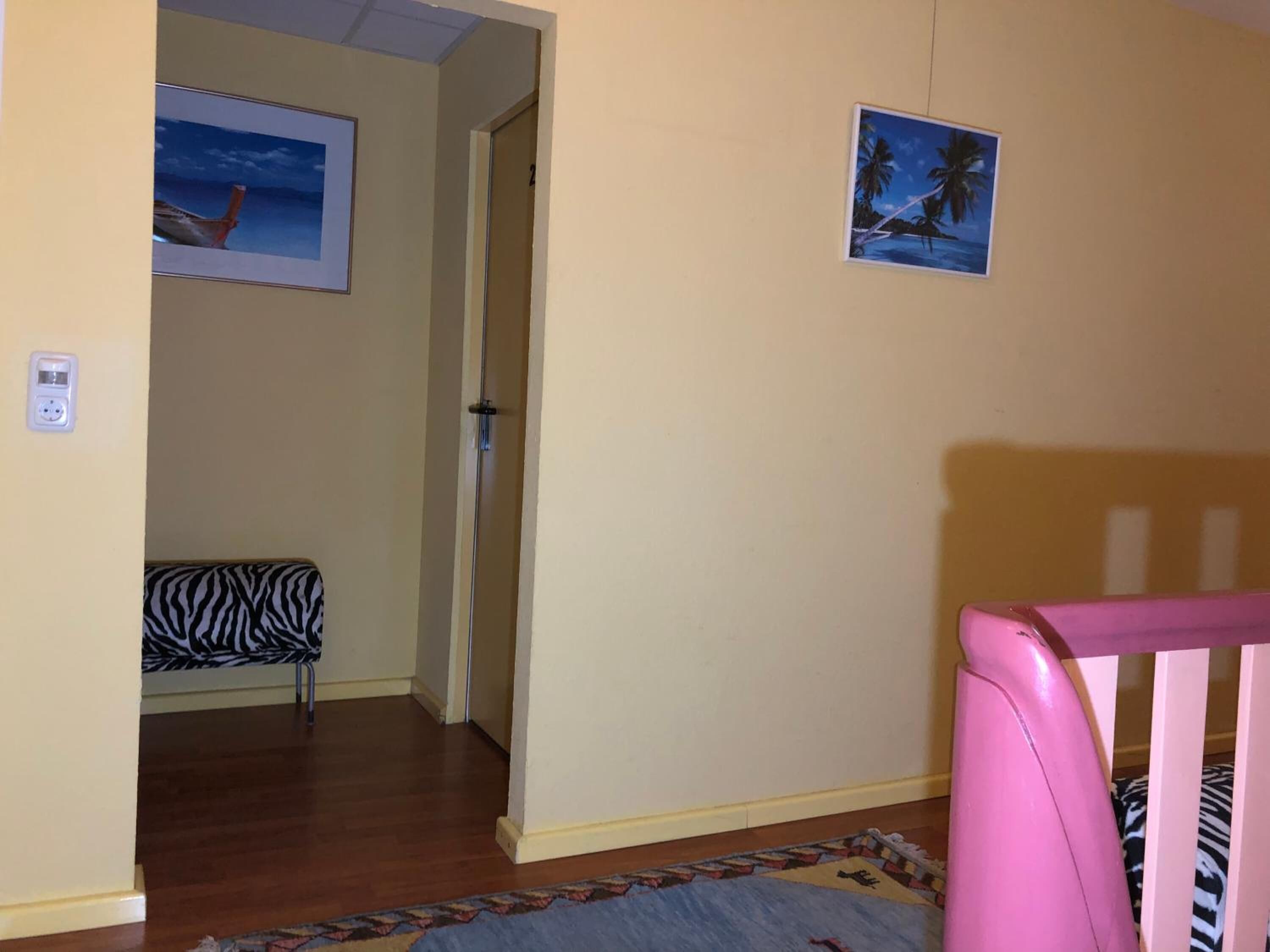 Une pièce avec un plancher en bois, une chaise à motifs zébrés, un berceau rose et deux tableaux encadrés accrochés au mur.