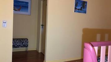 Une pièce avec un plancher en bois, une chaise à motifs zébrés, un berceau rose et deux tableaux encadrés accrochés au mur.