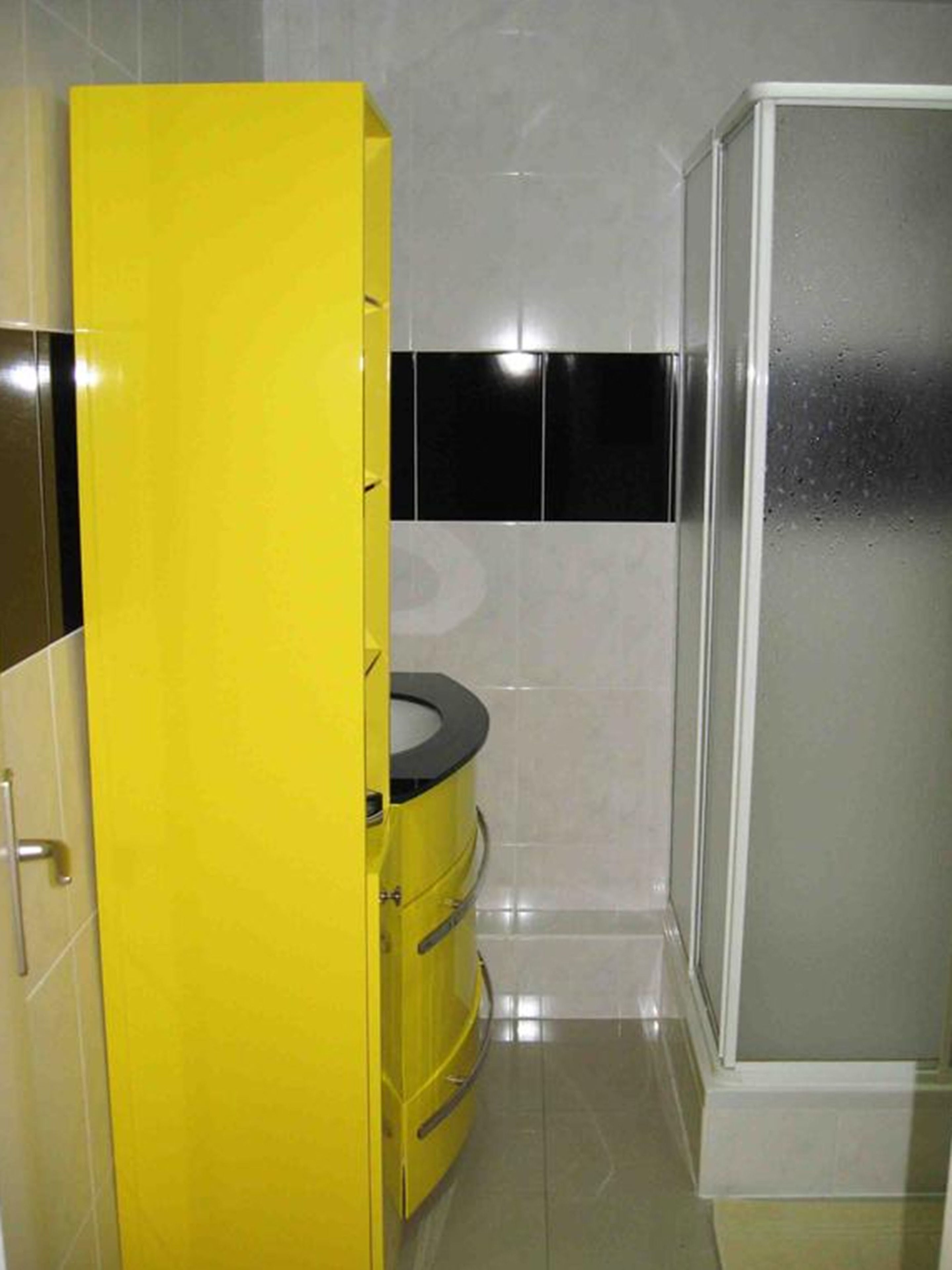 Um banheiro com um armário amarelo, vaso sanitário preto e box de vidro.