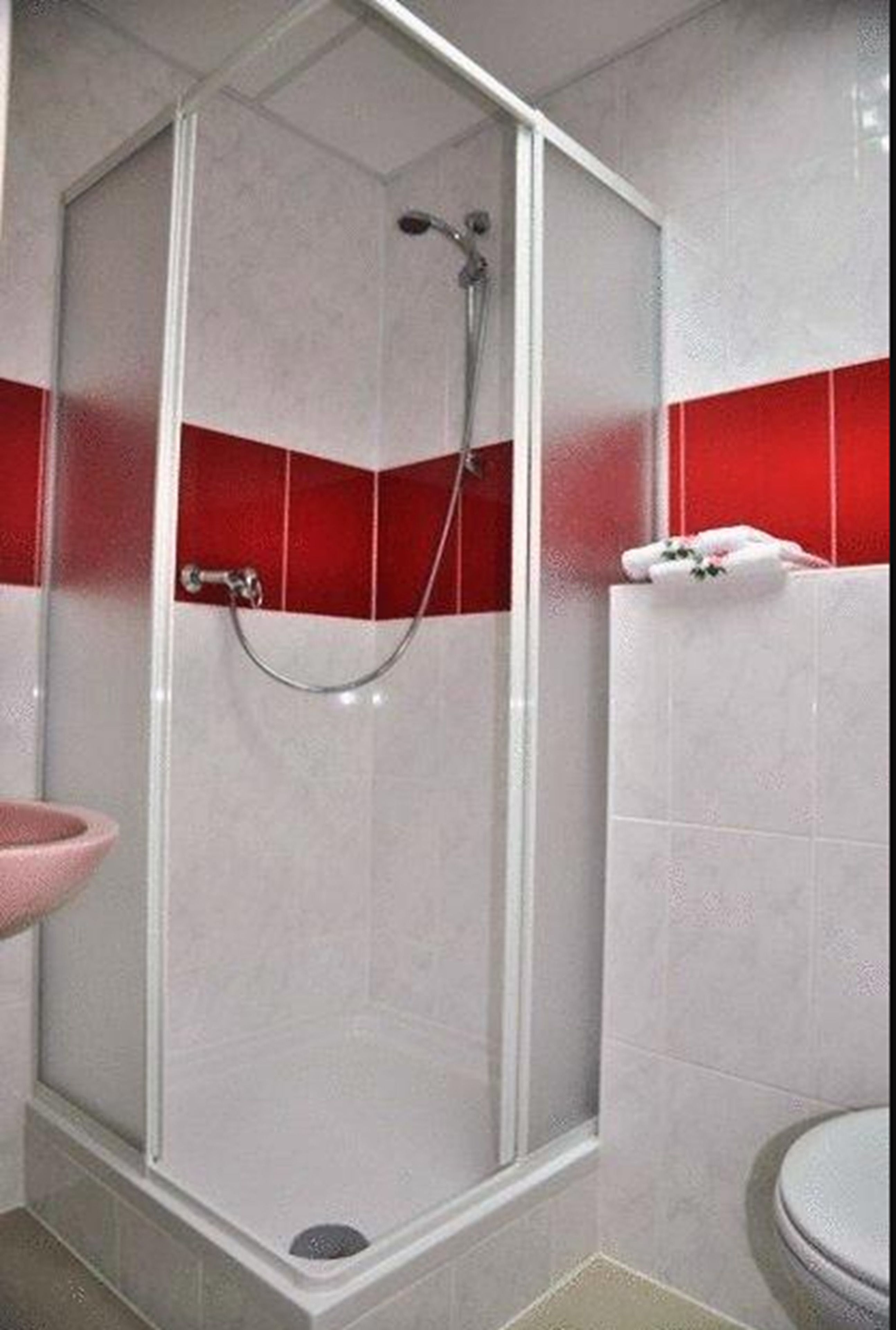 A shower with a glass door, a sink, and a toilet in a bathroom with red and white tiles.