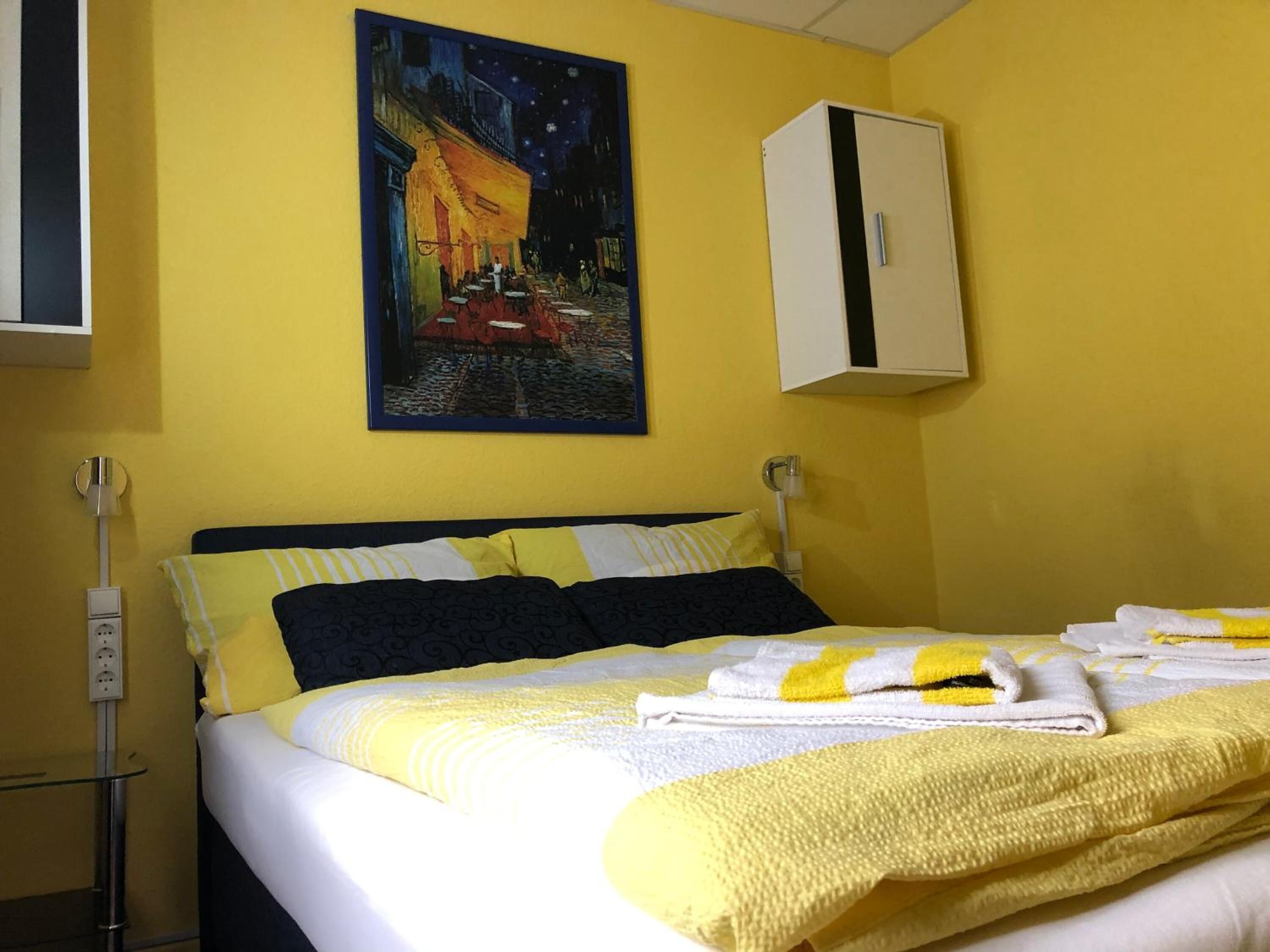 A hotel room with a bed, yellow walls, a painting of a night scene, and a white cabinet.