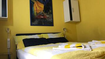 A hotel room with a bed, yellow walls, a painting of a night scene, and a white cabinet.