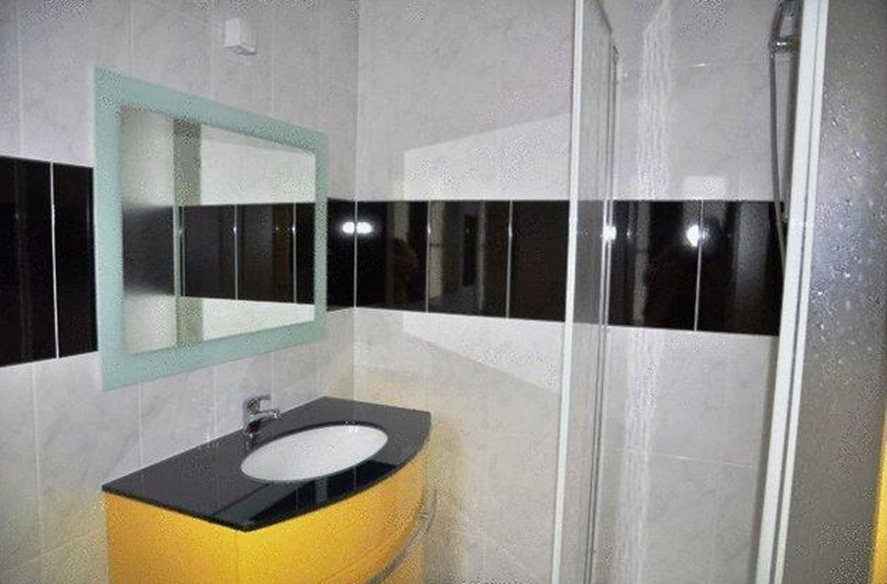 Ein Badezimmer mit Wandverkleidung aus schwarz-weißen Fliesen, einem gelben Waschbecken und einer Duschkabine aus Glas.