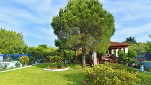 Un jardin bien entretenu, avec un grand arbre, un belvédère et une clôture bleue.