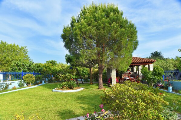 A well-maintained garden with a large tree, a gazebo, and a blue fence.
