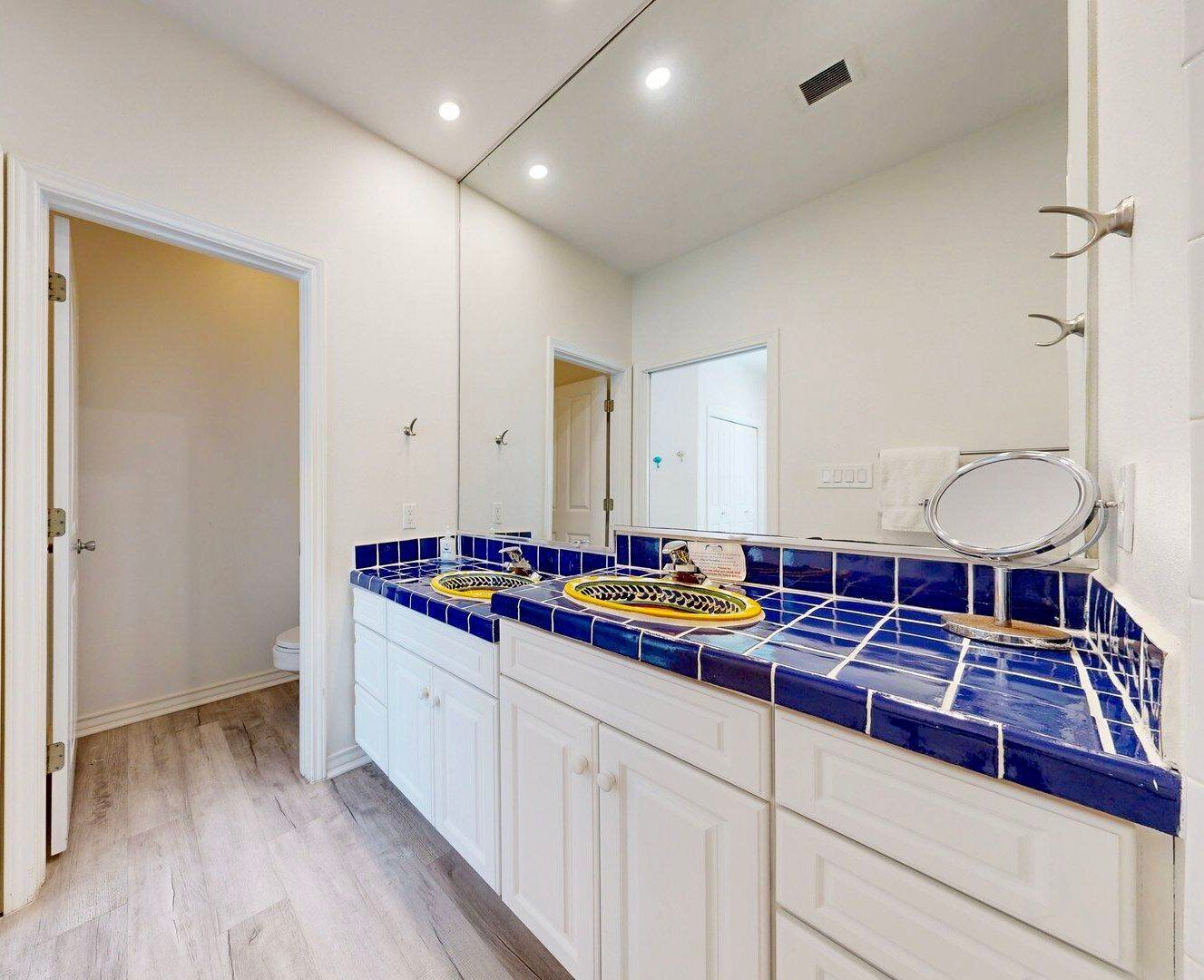 Un baño con armarios blancos, encimera con azulejos azules y un espejo grande.