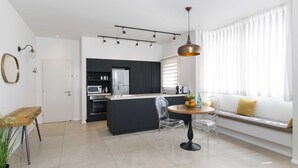 A modern kitchen with a central island, a dining area with a round table and chairs, and a seating area with a bench and cushions. - Tlv Center by Tlv2rent (Tel Aviv)