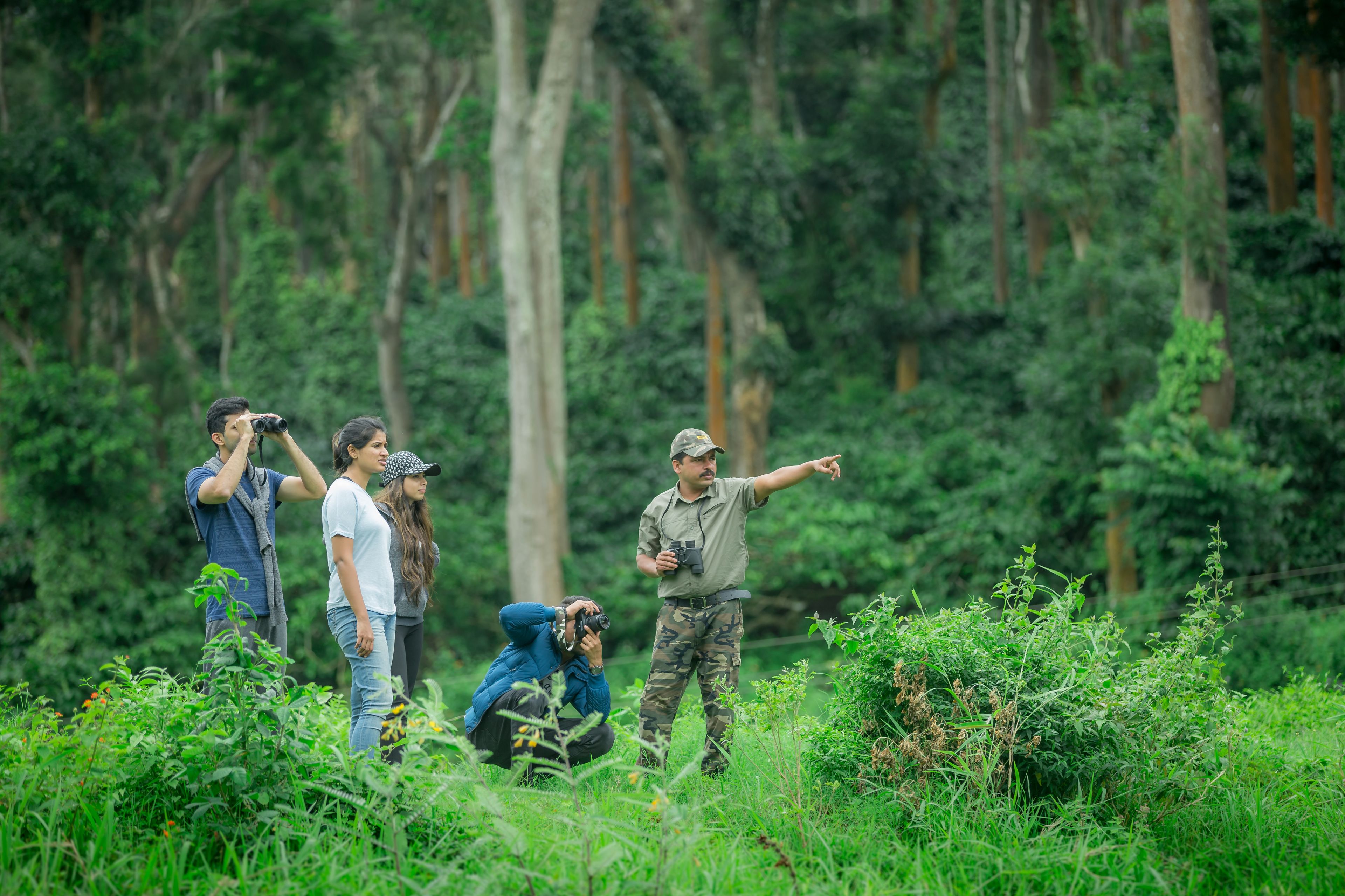 A group of people in a forested area, some taking photographs.