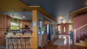 Una cocina amplia con armarios de madera, una zona de bar con taburetes y vistas al salón a través de una puerta abierta.