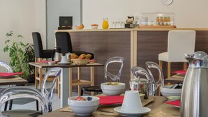 A modern breakfast area with clear chairs, a wooden counter with a coffee machine, and a clock on the wall.