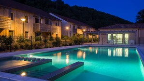 A swimming pool with steps leading into it, surrounded by a wooden building with balconies and a separate building with a patio area.