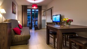 A furnished room with a sofa, a dining table, chairs, a TV, and a window with curtains.