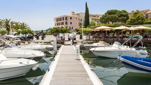 A marina with docked boats, a wooden pier, and a building with outdoor seating in the background.