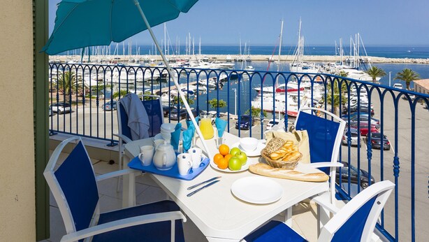 A balcony table with breakfast items, a view of the marina, and a clear blue sky.