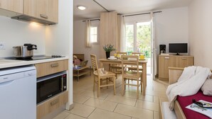 A compact kitchen with modern appliances, a dining area with wooden furniture, and a cozy living space with a bed and a TV.