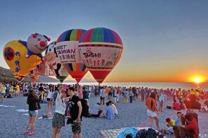 A beach with hot air balloons and a crowd of people.