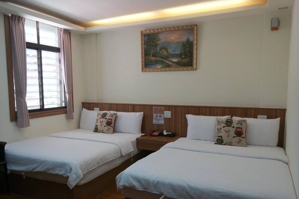 Una habitación de hotel con dos camas individuales, un cuadro en la pared y una ventana con cortinas.