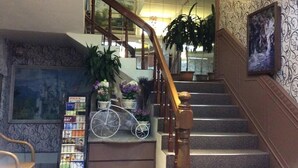Una escalera con barandilla de madera, una bicicleta decorativa blanca y una estantería con revistas.
