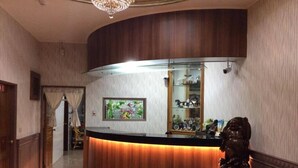 Un área de recepción con un mostrador curvo de madera, un candelabro y una estatua.