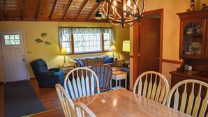 A cozy living room with a wooden dining table, white chairs, a blue armchair, and a sofa. - Cozy 2 bedroom cottage less than a mile to the beach (Dennis Port)