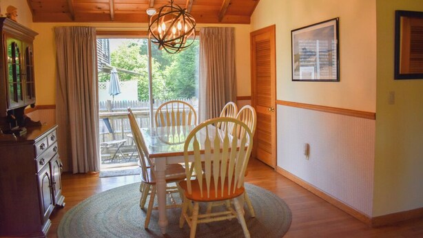 A dining area with a round table, four chairs, a chandelier, and a view through a glass door to the outside. - Cozy 2 bedroom cottage less than a mile to the beach (Dennis Port)