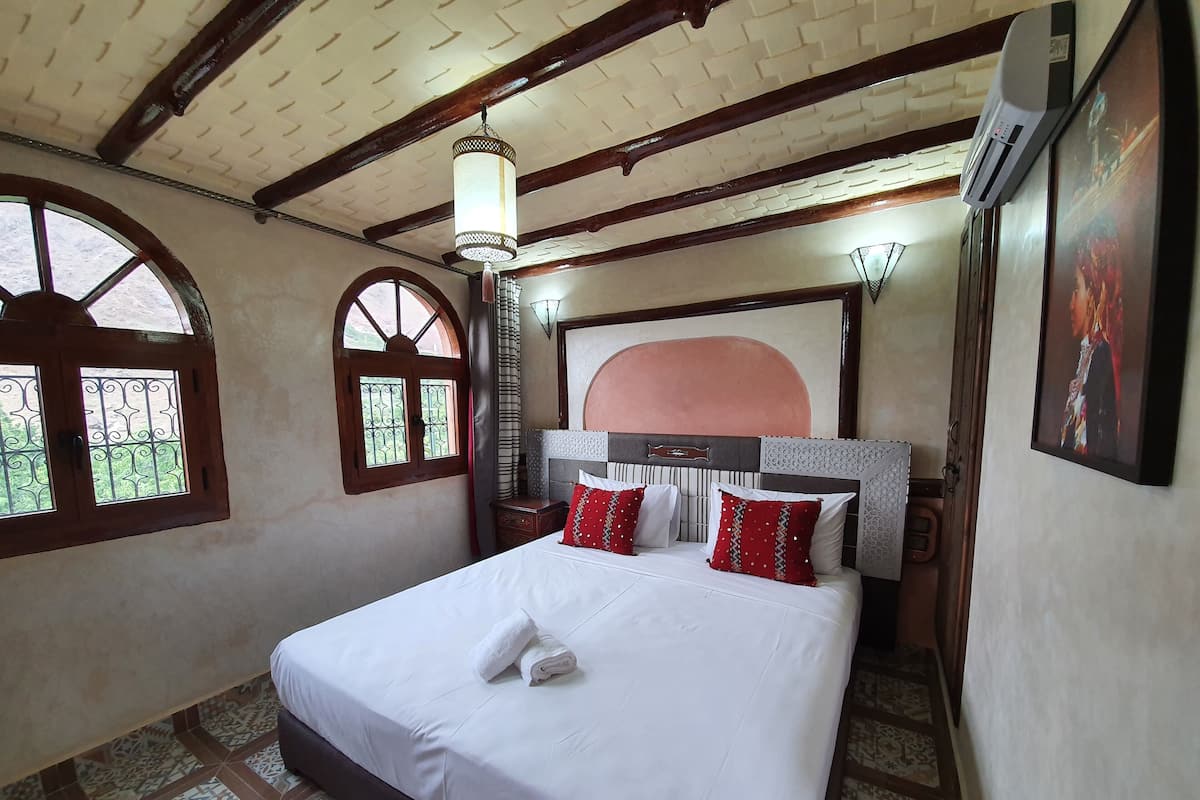 Quarto com cama grande, teto de madeira, janela com vista e ar condicionado fixado na parede.