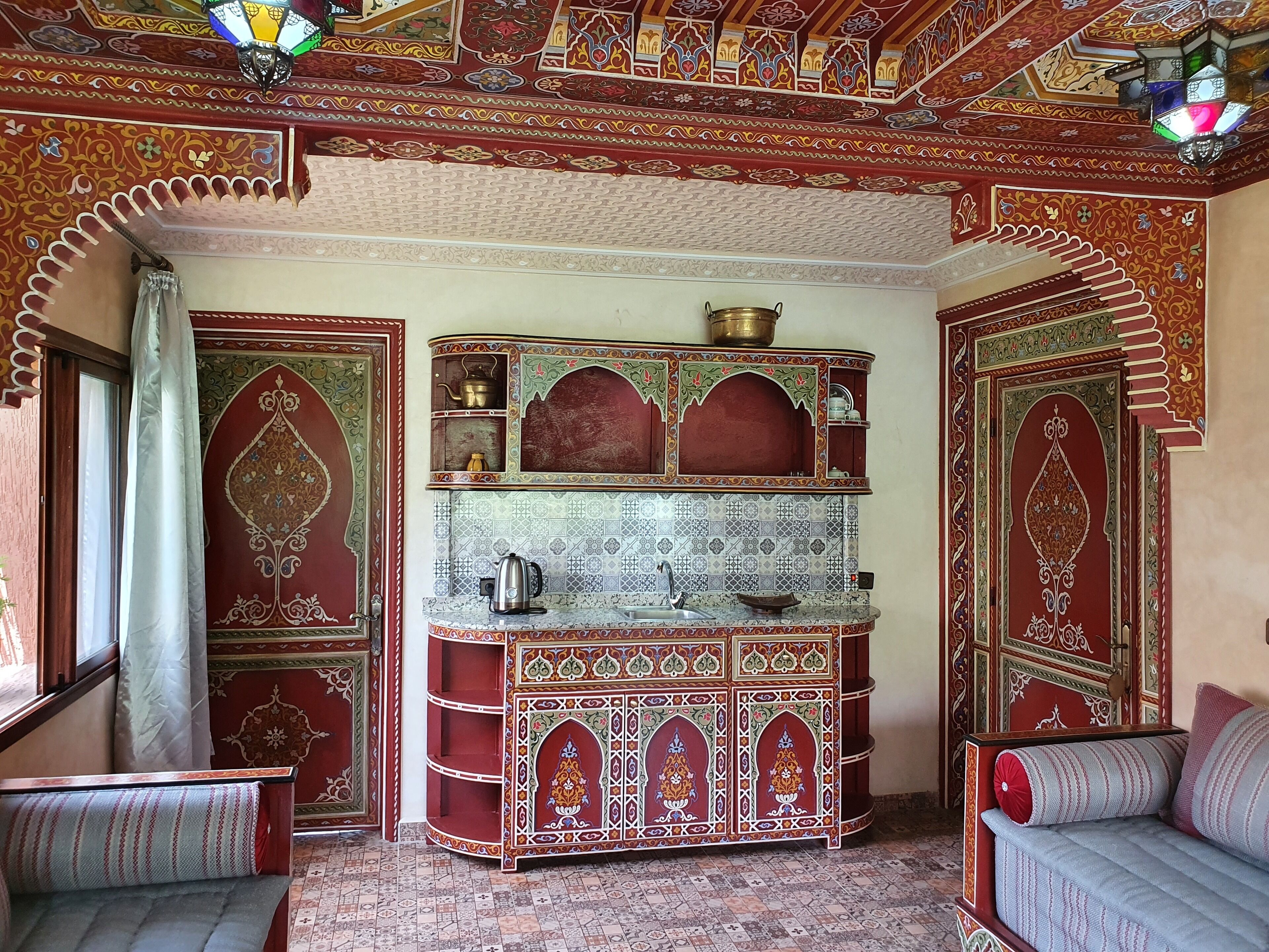 Una habitación tradicional con un papel tapiz estampado, una zona de cocina integrada y un rincón de estar con cojines.