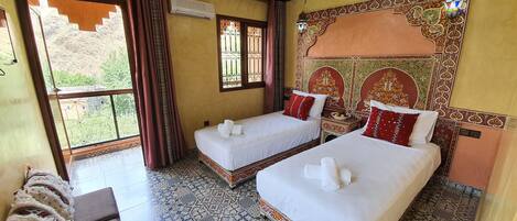 Habitación de hotel con dos camas, un ventanal con cortinas, suelo estampado y una pared decorativa.