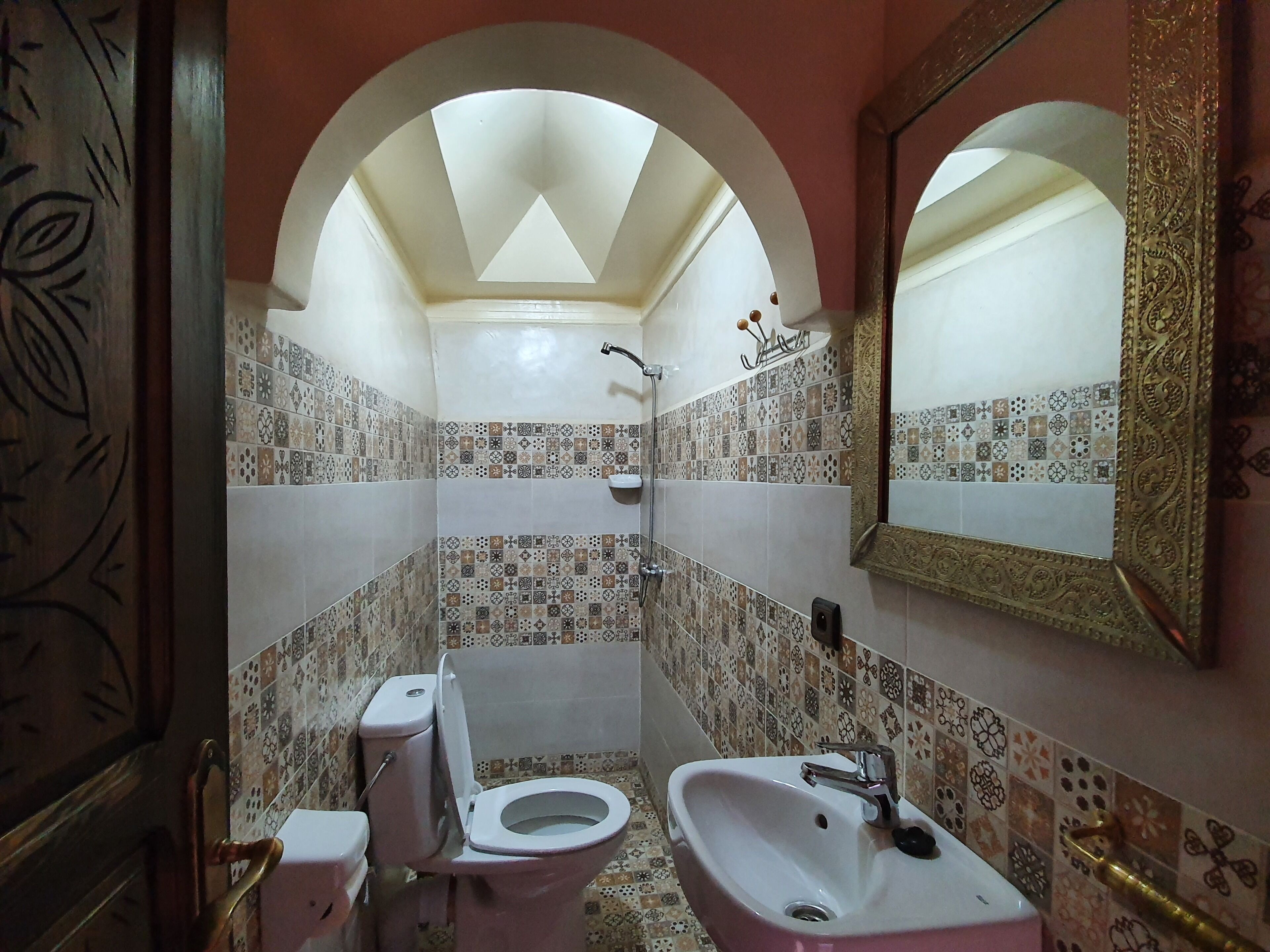 Un baño con inodoro, lavabo, ducha y espejo con marco decorativo.