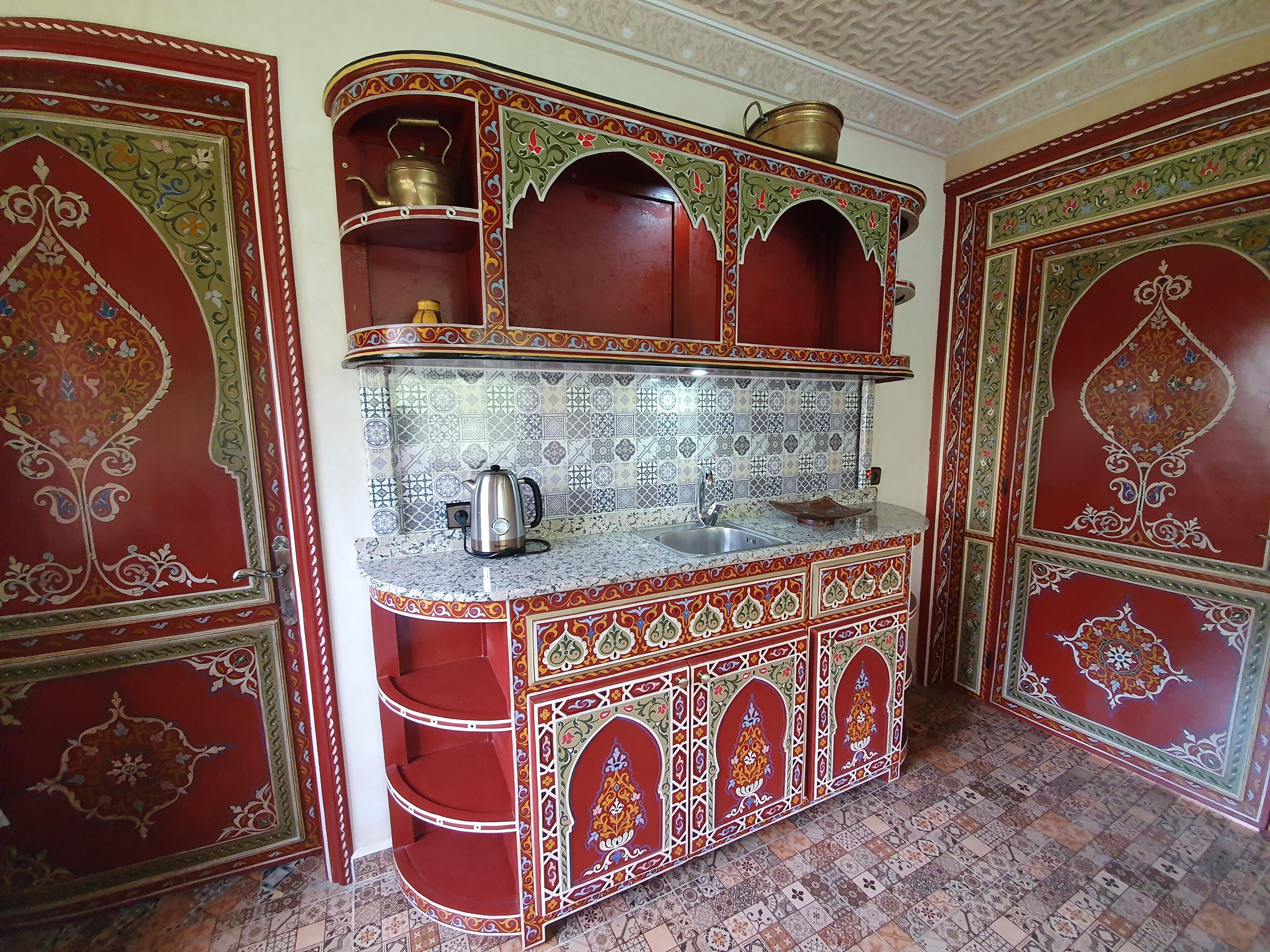 Une cuisine traditionnelle avec des meubles richement décorés, un pare-feu en carreaux et une bouilloire en acier inoxydable.
