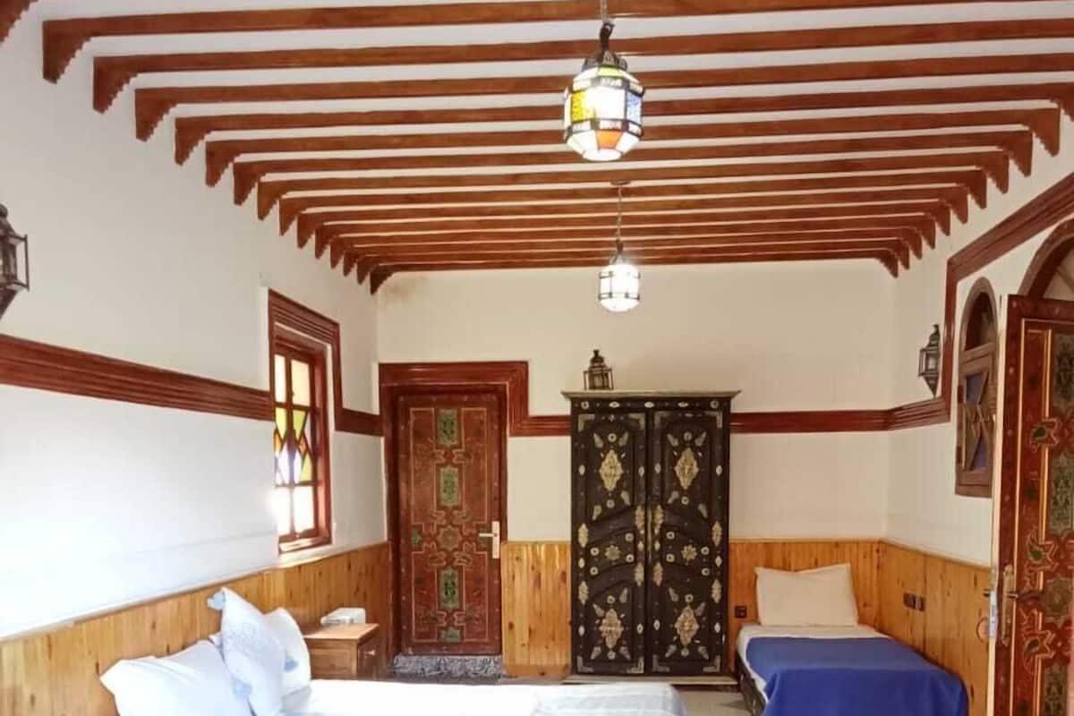 Quarto com uma cama grande, duas camas menores, vigas de madeira no teto e uma porta decorativa.