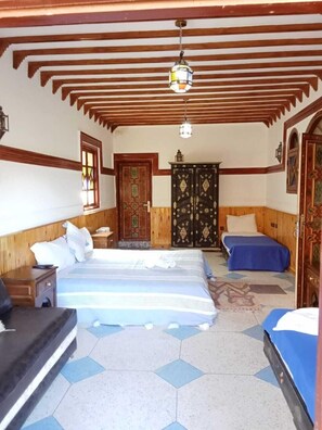 A room with a large bed, two smaller beds, wooden beams on the ceiling, and a decorative door. - Dar Assarou (Asni)
