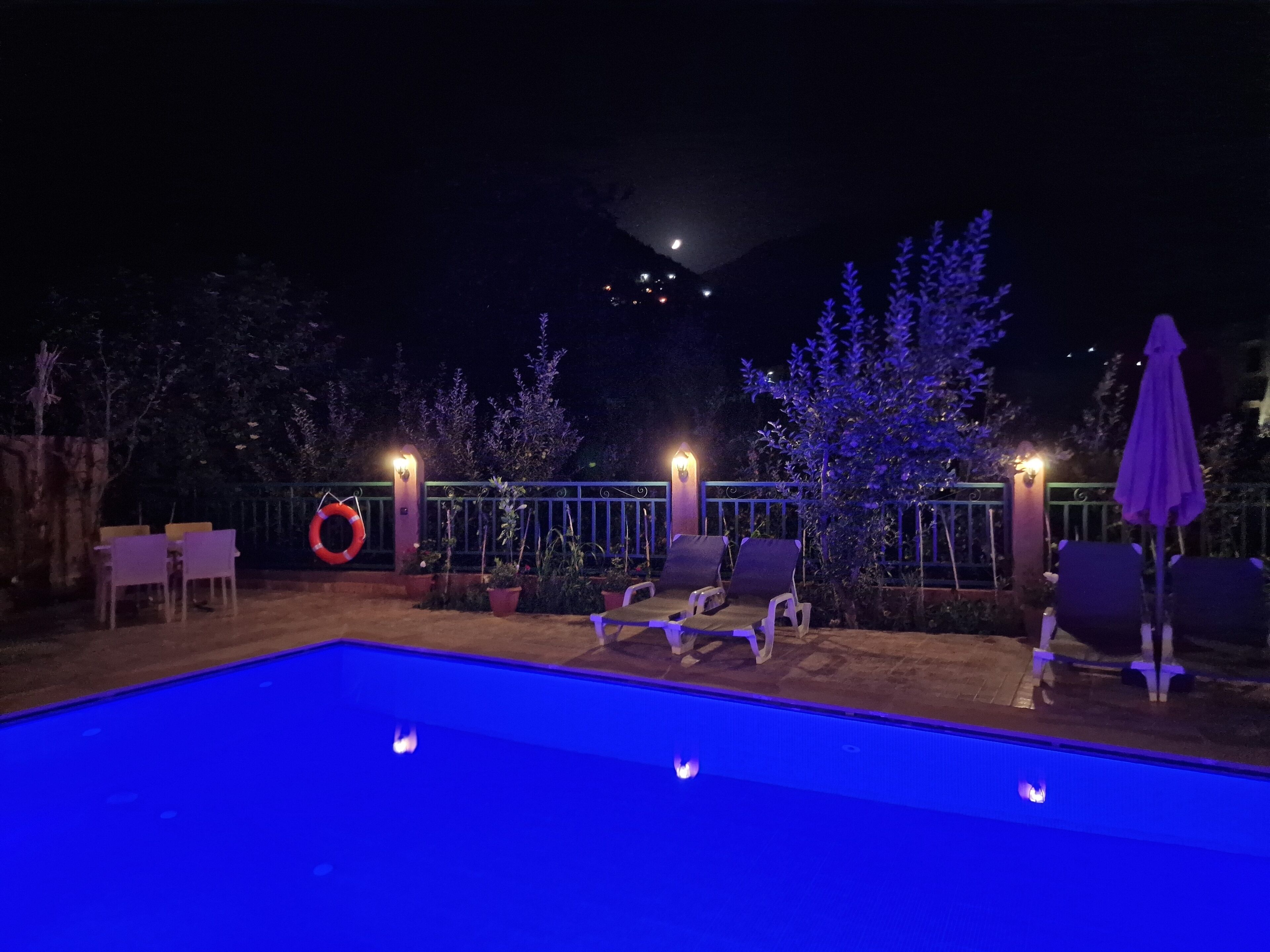 Uma área de piscina com espreguiçadeiras e um salva-vidas preso a uma grade.
