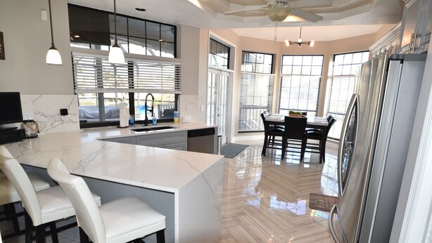 A modern kitchen with a marble island, stainless steel appliances, and a dining area with a view. - Villa Oasis, w/Heated & Covered Pool, Pool Table, Boat Dock, Gym and much more. (Apollo Beach)