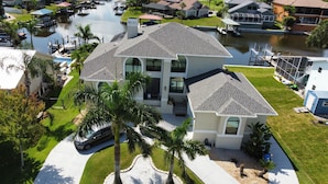 A two-story house with a garage, a swimming pool, and a dock extending into a body of water. - Villa Oasis, w/Heated & Covered Pool, Pool Table, Boat Dock, Gym and much more. (Apollo Beach)