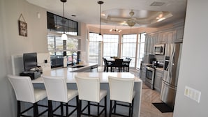 A modern kitchen with a central island, bar stools, and stainless steel appliances. - Villa Oasis, w/Heated & Covered Pool, Pool Table, Boat Dock, Gym and much more. (Apollo Beach)
