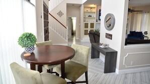 A dining area with a round table and chairs, a staircase, and a living room with a sofa and a coffee table. - Villa Oasis, w/Heated & Covered Pool, Pool Table, Boat Dock, Gym and much more. (Apollo Beach)