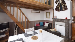 Um quarto com escada de madeira, mesa de jantar com toalha branca, televisão e lareira.